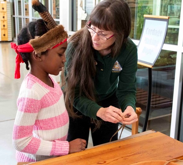 An MDC staff member teaches a little girl how to make cordage from plant fibers.