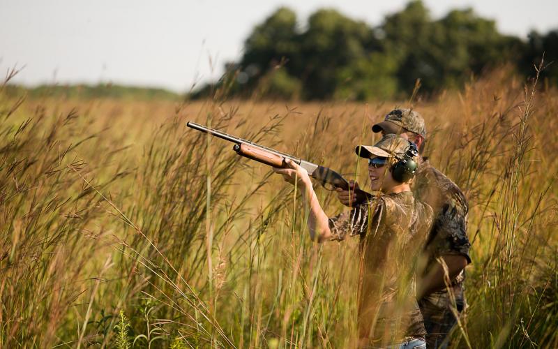 young hunter in field shoots at doves while other hunter watches