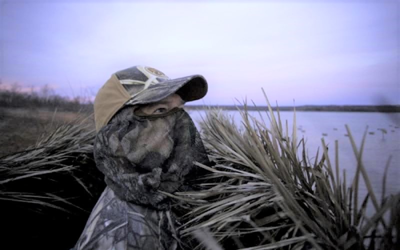 camouflaged male duck hunter in duck blind