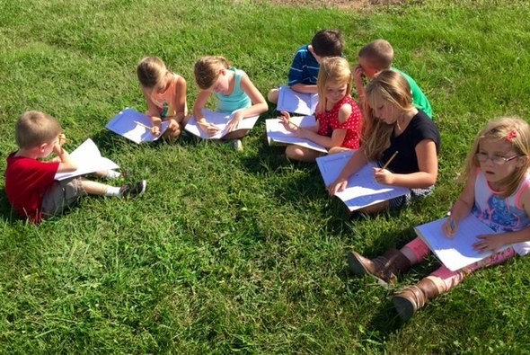 Young students sitting in grass learning about nature outside 