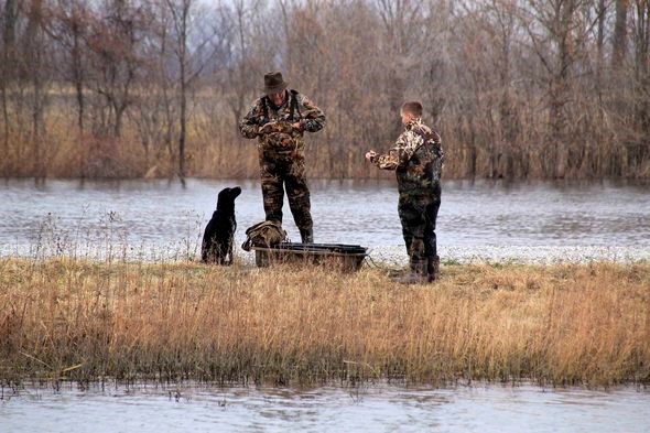 two waterfowl hunters with a dog prepare to hunt