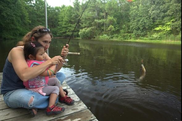 Lady helping a little girl catch a fish.