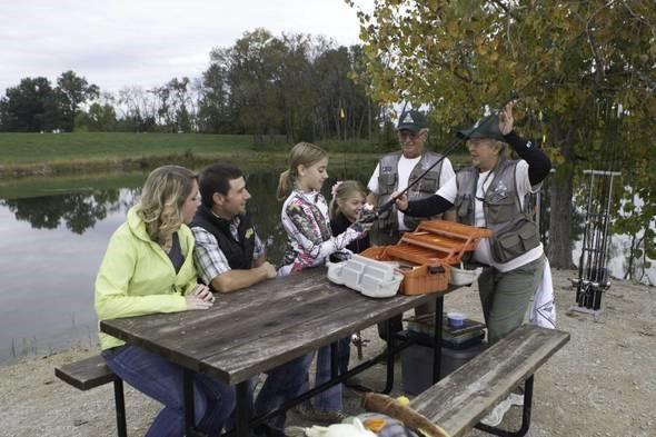Two volunteers teach Discover Nature Fishing class to family at picnic table 
