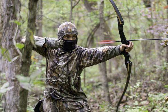 A bowhunter releases his arrow in the woods.