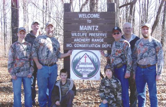 Eight members of On Target Archers pose in front of the Maintz Conservation Area sign.