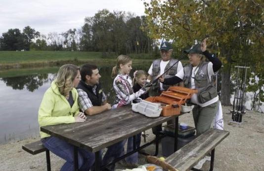 Two volunteers teach Discover Nature Fishing class to family at picnic table 
