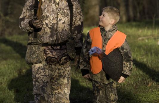 man and boy walking in woods with turkey decoy