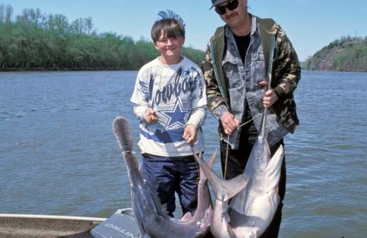 man and boy on boat with two paddlefish