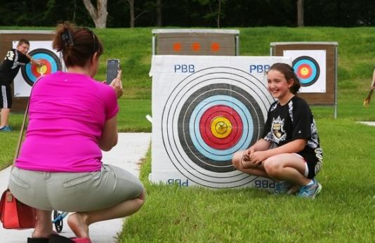 a woman takes a picture of a girl with an archery target and bulls-eye arrow