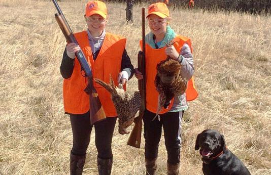 two upland bird hunters holding harvested pheasants with dog
