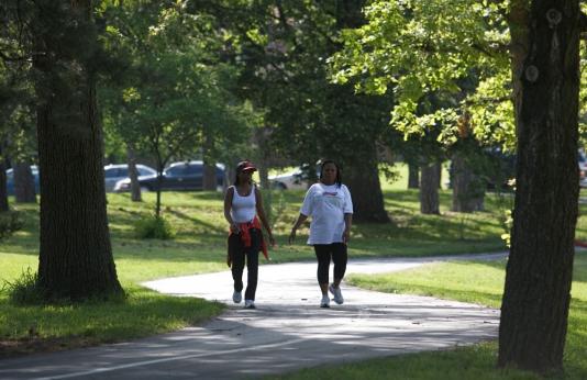 two women walk along sidewalk under mature urban trees
